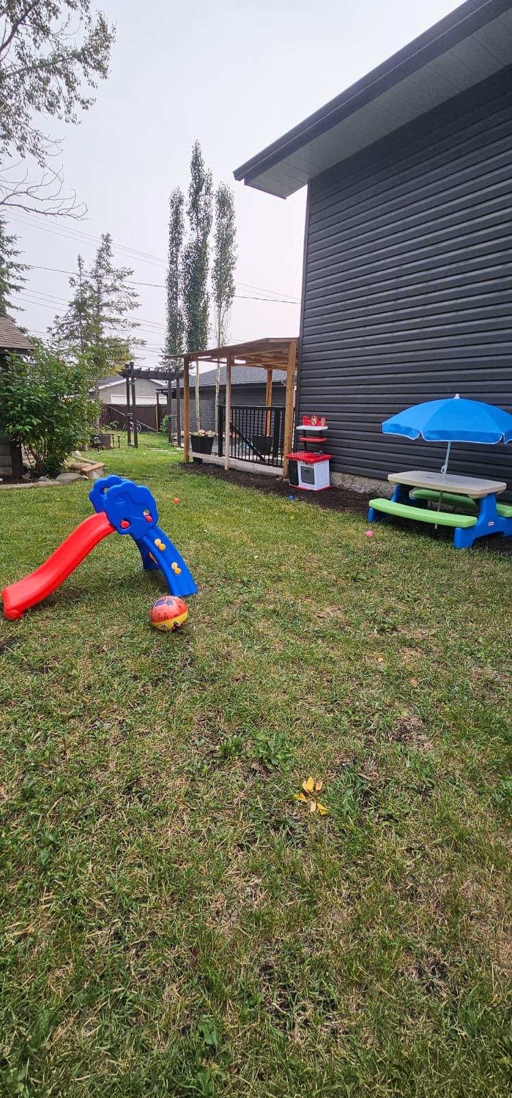 Backyard play area with green lawn, colorful slide, and outdoor toys at MJ Play House Day Home